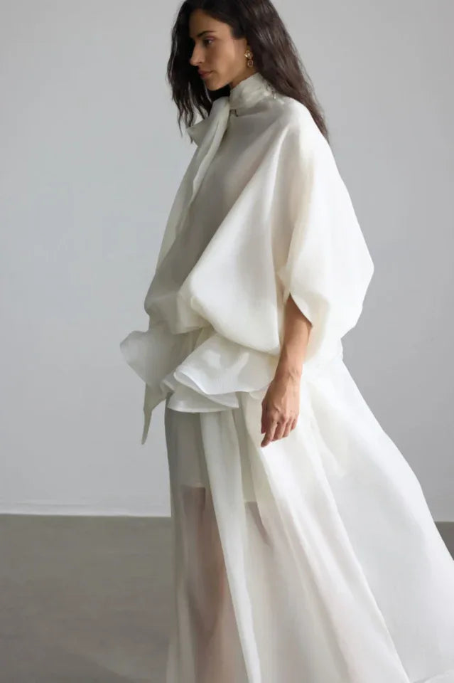 Close-up on the upper body of a woman in a white designer dress, highlighting the unique neckline and sleeve construction.