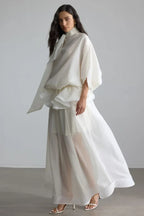 Woman modeling a modern white formal dress with a flowing silhouette and a sheer, layered skirt.