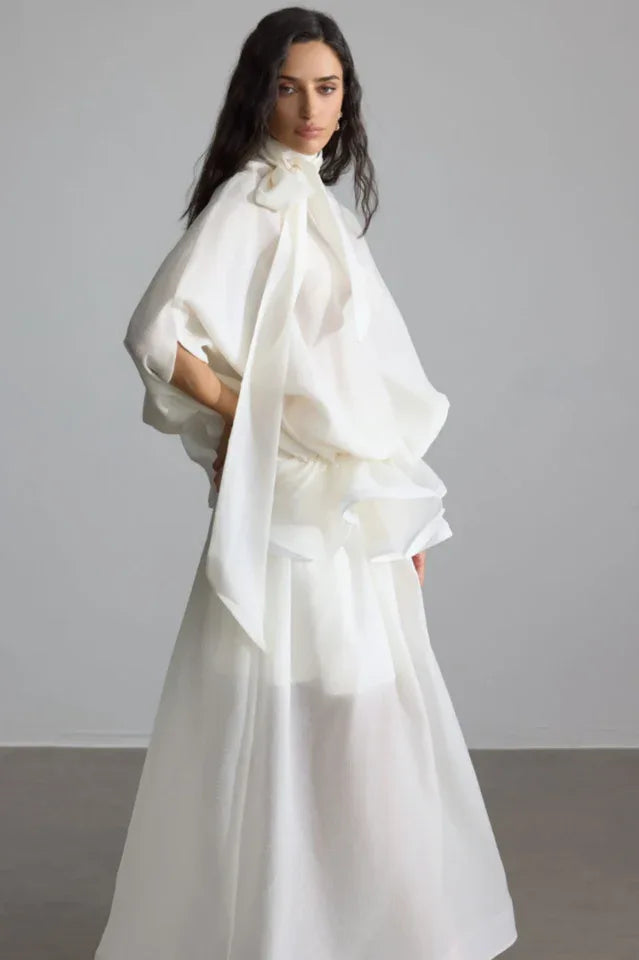 Side profile of a woman in an elegant white gown, showcasing the draped sleeves and ruffled waist detail.