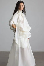 Side profile of a woman in an elegant white gown, showcasing the draped sleeves and ruffled waist detail.