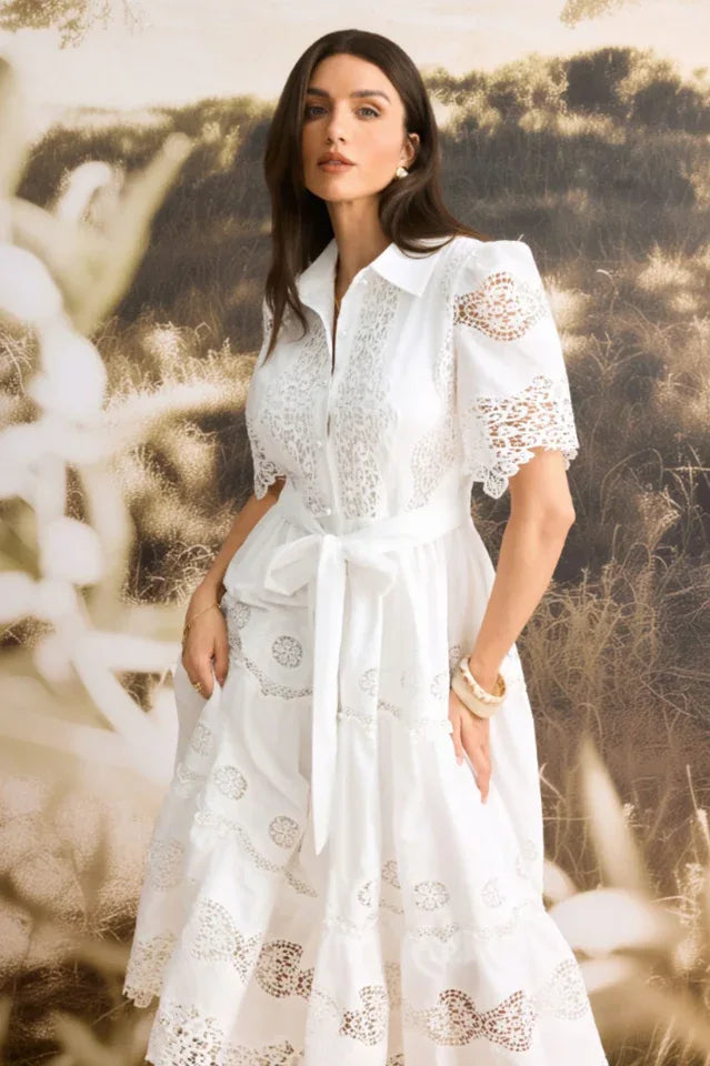 Close-up of a woman wearing a white lace midi dress, showcasing the intricate details and belted waist.