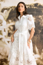 Close-up of a woman wearing a white lace midi dress, showcasing the intricate details and belted waist.