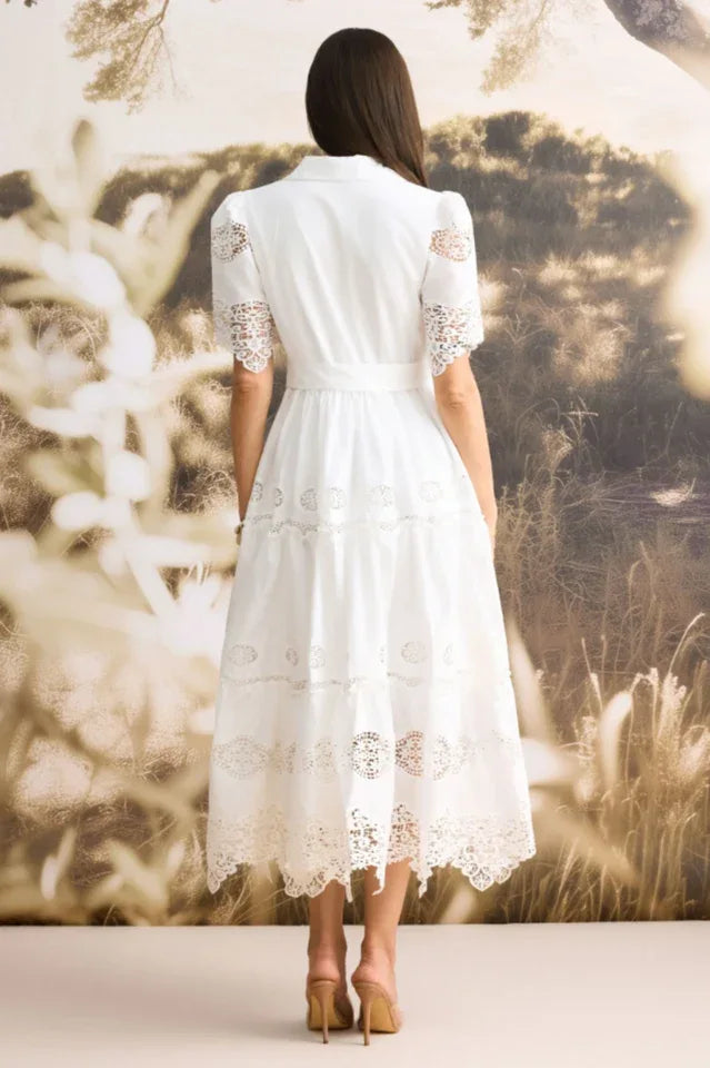 Back view of a woman wearing a white lace midi dress with a tiered skirt and short sleeves.