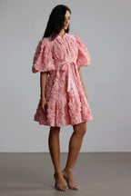 Model posing in a short pink textured dress with voluminous sleeves and a flared skirt