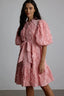 Woman wearing a pink textured dress with puff sleeves and a belted waist