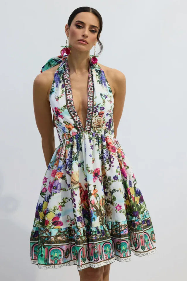 Side view of a woman in a floral print halter mini dress, showcasing the open back and flowing skirt. Secondary image