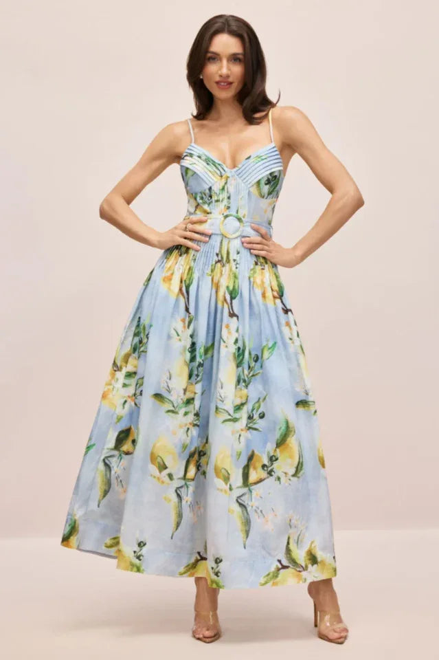 Woman wearing a light blue midi dress with a lemon print, spaghetti straps, a sweetheart neckline, and a full skirt.