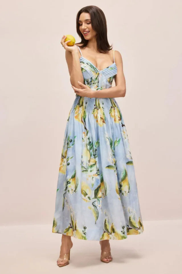 Woman in a light blue midi dress with a lemon print, holding a lemon.