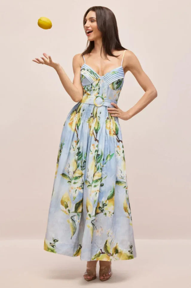 Woman in a light blue midi dress with a lemon print, tossing a lemon.