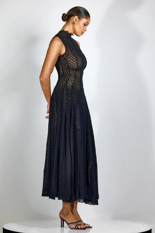 Side profile of a woman in a black textured knit midi dress with a mock neck