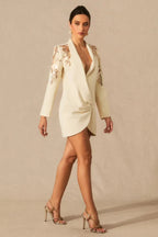 Woman walking in a cream tuxedo dress with embellished shoulders and high heels.