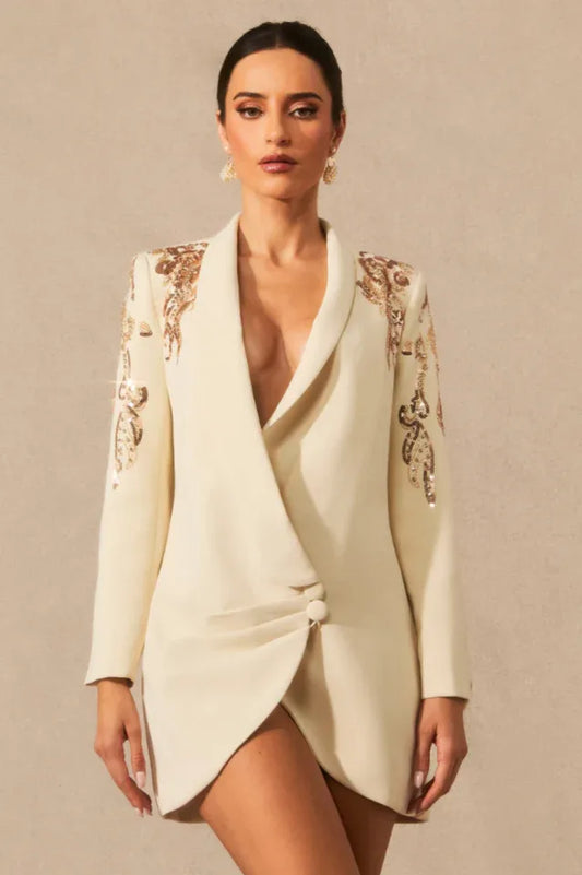Woman wearing a cream tuxedo dress with embellished shoulders and a deep V-neckline.