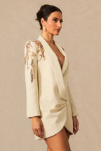 Side view of a woman in a cream tuxedo dress with embellished shoulders.
