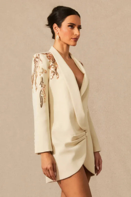 Side view of a woman in a cream tuxedo dress with embellished shoulders.