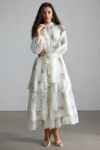 Woman wearing a white floral print chiffon tiered midi dress with long bishop sleeves and a high neckline.