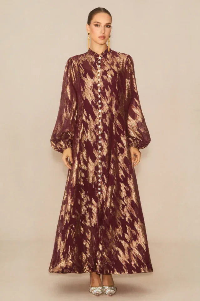 Front view of a model in a burgundy and gold printed maxi dress with a high neckline and button-down front. Secondary image