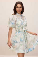 Woman looking at the camera wearing a white floral print mini dress with puff sleeves and a belted waist