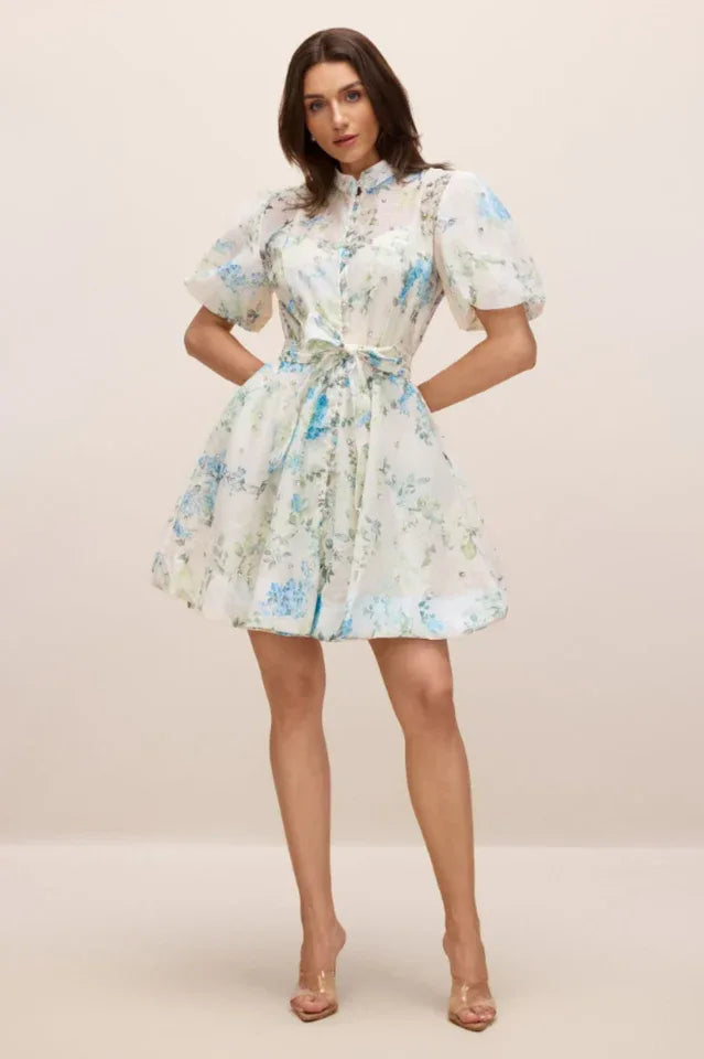 Full body shot of a woman wearing a white floral print mini dress with puff sleeves and a belted waist