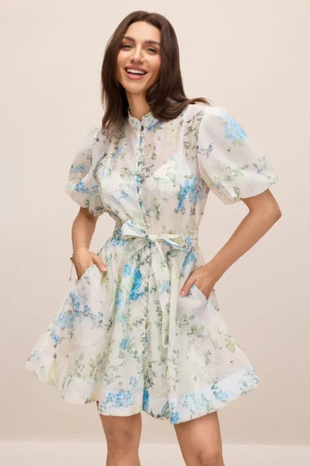 Woman smiling wearing a white floral print mini dress with puff sleeves and a belted waist