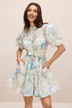 Woman smiling wearing a white floral print mini dress with puff sleeves and a belted waist