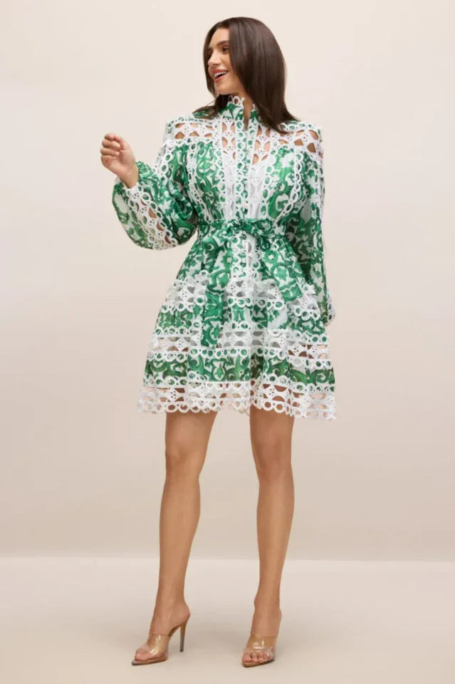 Woman in a green and white cut-out mini dress with lace trim, smiling and gesturing. Secondary image