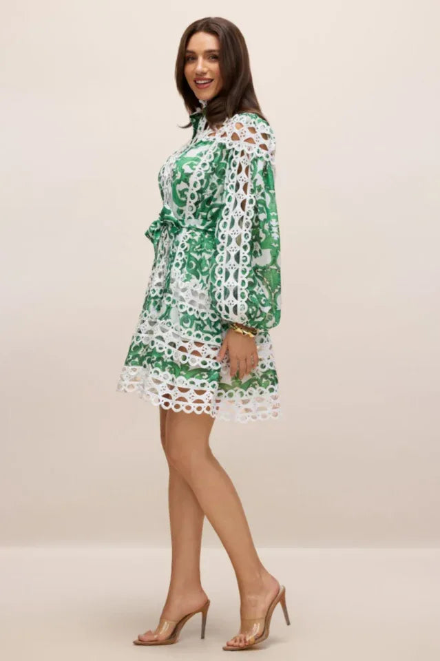 Three-quarter side view of a woman wearing a green and white cut-out mini dress with lace details and clear heels.