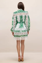 Back view of a woman wearing a green and white cut-out mini dress with long puff sleeves and lace trim.
