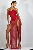 Woman in a red strapless gown with fringe and high slits, standing with one leg forward.