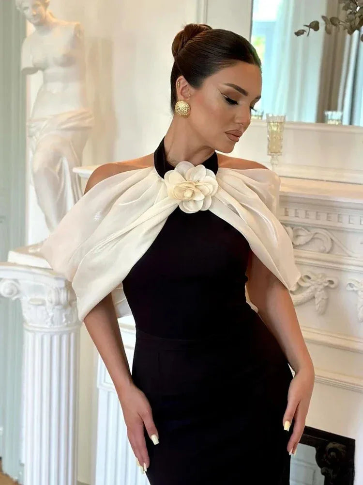 Close-up of a woman wearing a black sheath dress with a white sheer off-the-shoulder overlay and flower accent, showcasing the neckline and details.
