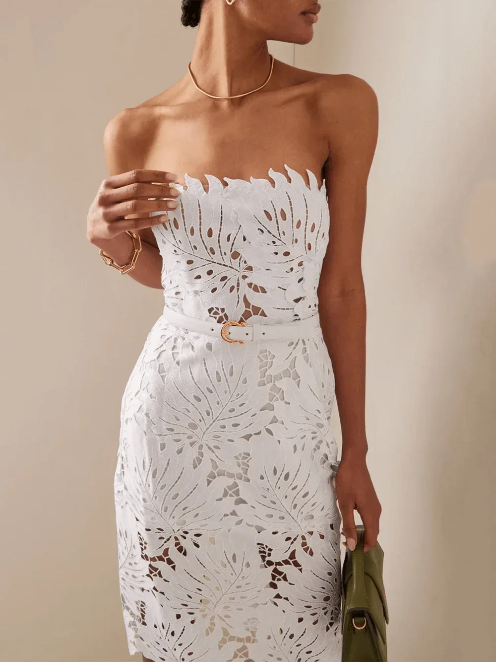Woman wearing a white strapless lace sheath dress with leaf cutouts and a white belt.