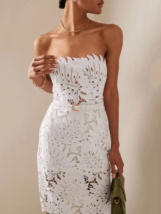 Woman wearing a white strapless lace sheath dress with leaf cutouts and a white belt.