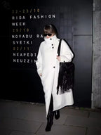 Woman in a white oversized wool blend coat with a black fringed bag
