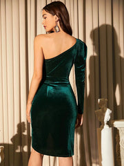 Rear view of a woman in an emerald green velvet one-shoulder dress, showcasing the back of the garment and its fitted silhouette.