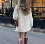 back view of a woman in a cream faux fur coat and brown boots