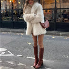 full shot of a woman in a cream faux fur coat and brown boots