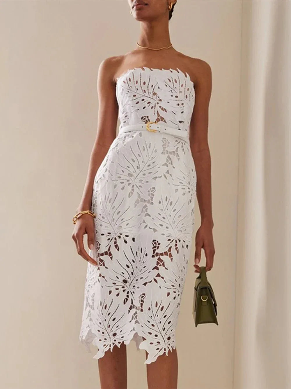 Close-up of a woman wearing a white strapless lace dress with intricate leaf cutouts and a gold necklace.