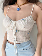 Front view of a woman wearing a white eyelet camisole top with blue floral accents and a tie-front detail.