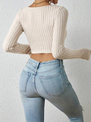 Back view of a woman wearing a cream-colored ribbed long-sleeve crop top and light-wash denim jeans.