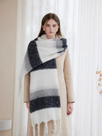 Woman wearing a cream coat and a large, striped scarf draped over her shoulders, featuring white, grey, and dark blue bands.