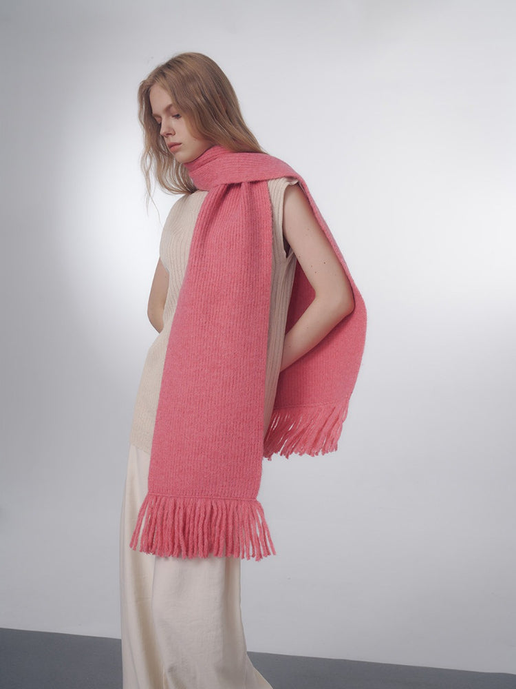 Model wearing a pink knitted scarf with fringe detailing draped over her shoulders.