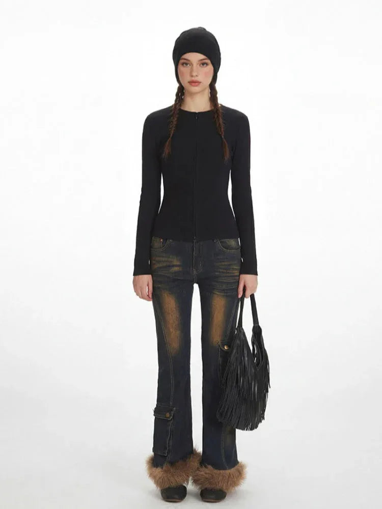 Model wearing a black ribbed knit top, distressed flared jeans with fur trim cuffs, and a black beanie, holding a fringe detail bag.