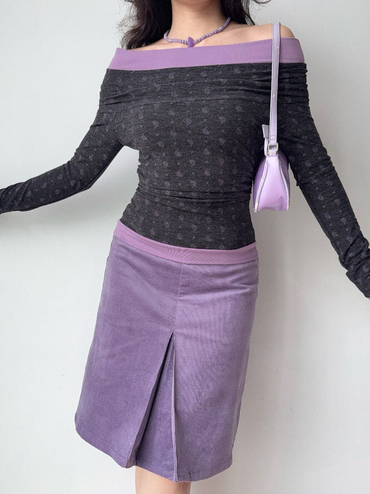 Full body shot of a woman wearing a grey and purple off-the-shoulder long-sleeve top and a matching skirt, holding a small purple handbag.