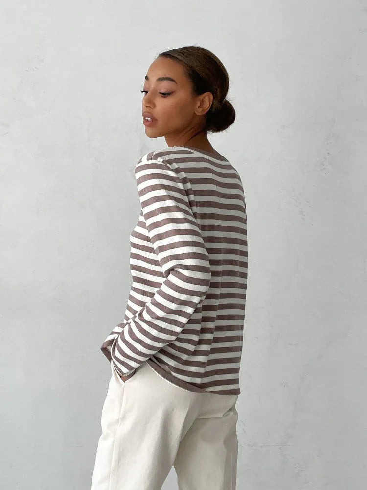 Side view of a woman wearing a brown and white striped long-sleeved crew neck sweater with cream-colored pants. Secondary image