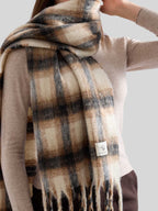Detail shot of the plaid pattern and fringe on an oversized scarf worn by a woman.