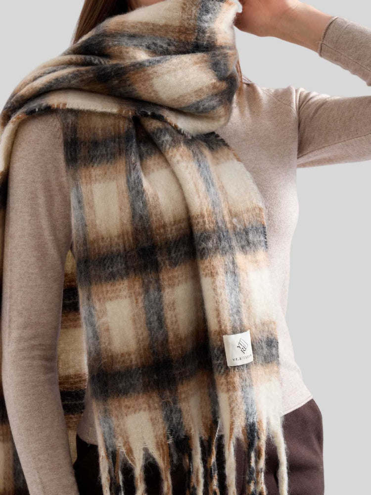 Detail shot of the plaid pattern and fringe on an oversized scarf worn by a woman.