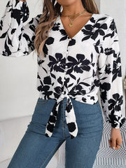 Woman wearing a black and white floral print long sleeve blouse with a front tie detail and blue jeans, posing, front view