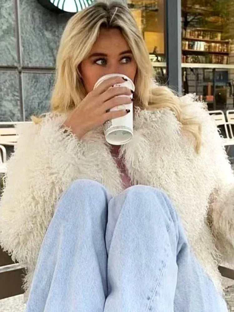 Woman wearing a white shaggy faux fur cropped jacket and light blue jeans, holding a coffee cup. Main image