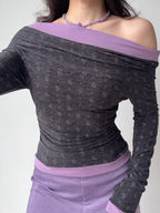 Close-up of a woman wearing a grey and purple off-the-shoulder long-sleeve top with a floral print.