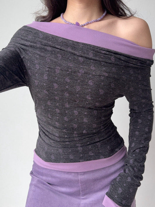 Close-up of a woman wearing a grey and purple off-the-shoulder long-sleeve top with a floral print.