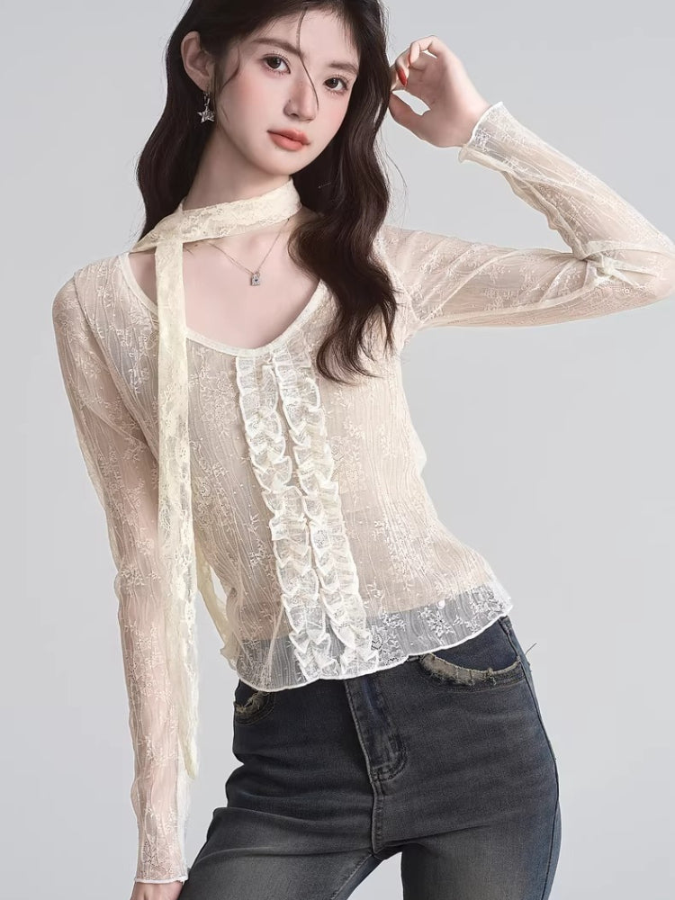 Front view of a woman in a cream lace top with ruffled front and a long scarf hanging down.